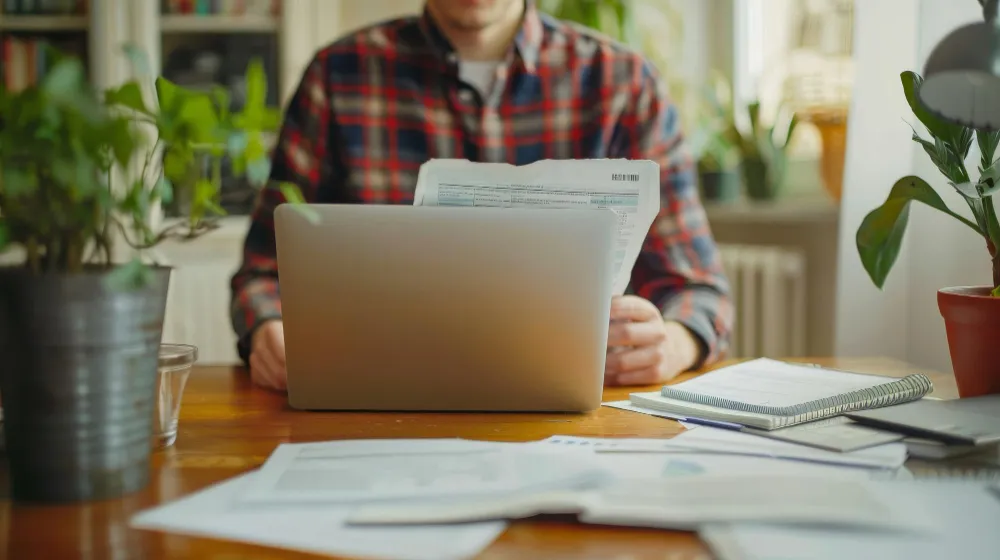 Persoană care verifică documente contabile și introducere date la laptop