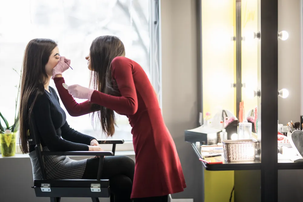 Makeup artist realizând un machiaj profesional unei cliente într-un salon de înfrumusețare.