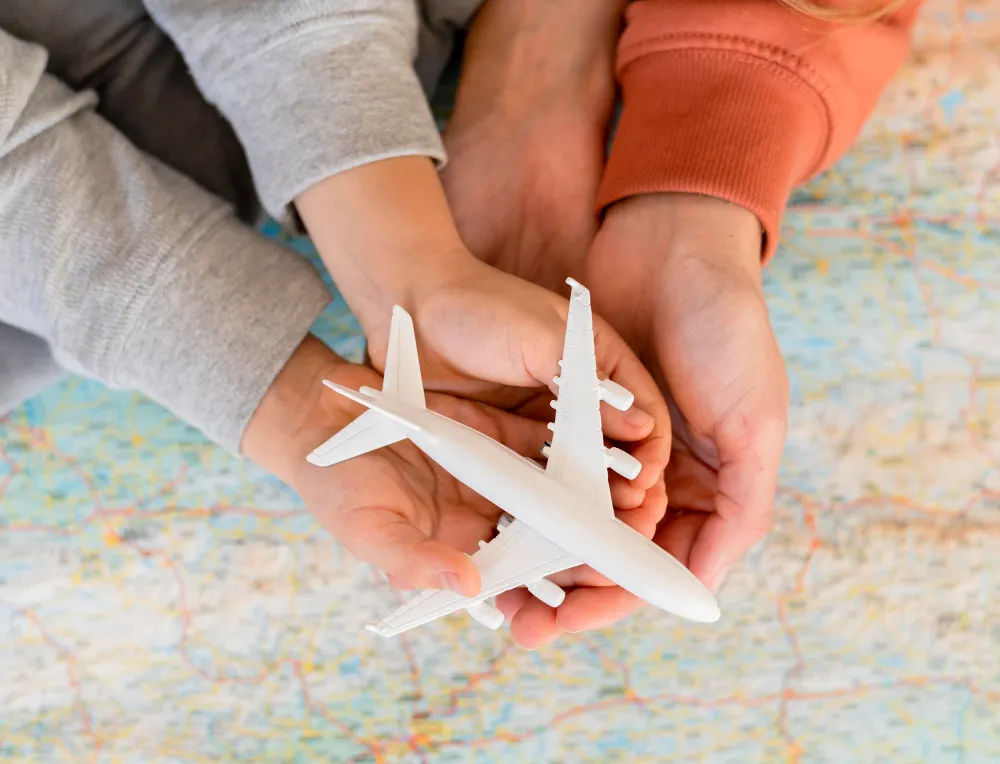 Mâinile unui părinte și copil cu un avion de jucărie pe hartă, planificând o călătorie asigurată