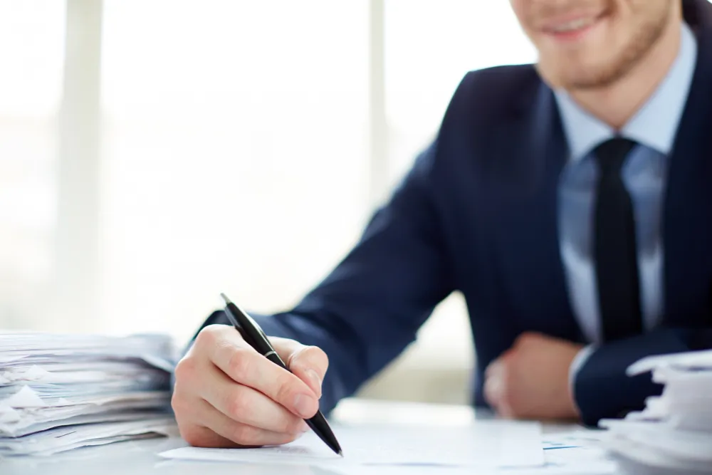 Consultant în costum care completează documente juridice la birou, lângă teancuri de dosare