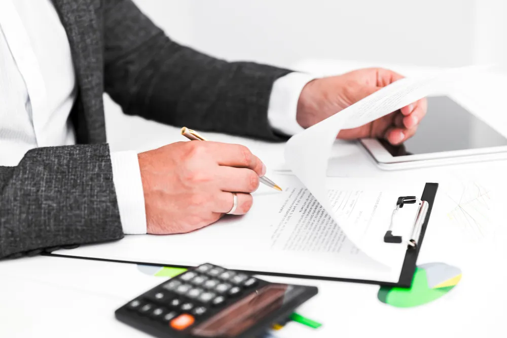 Bărbat care completează documente fiscale lângă un calculator, pentru calculul impozitului pe veniturile microîntreprinderii